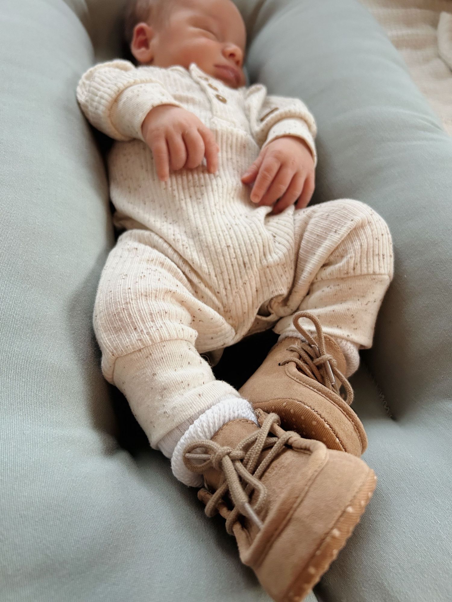 Close-up of sleeping newborn in cream ribbed romper wearing tan lace-up baby boots.
