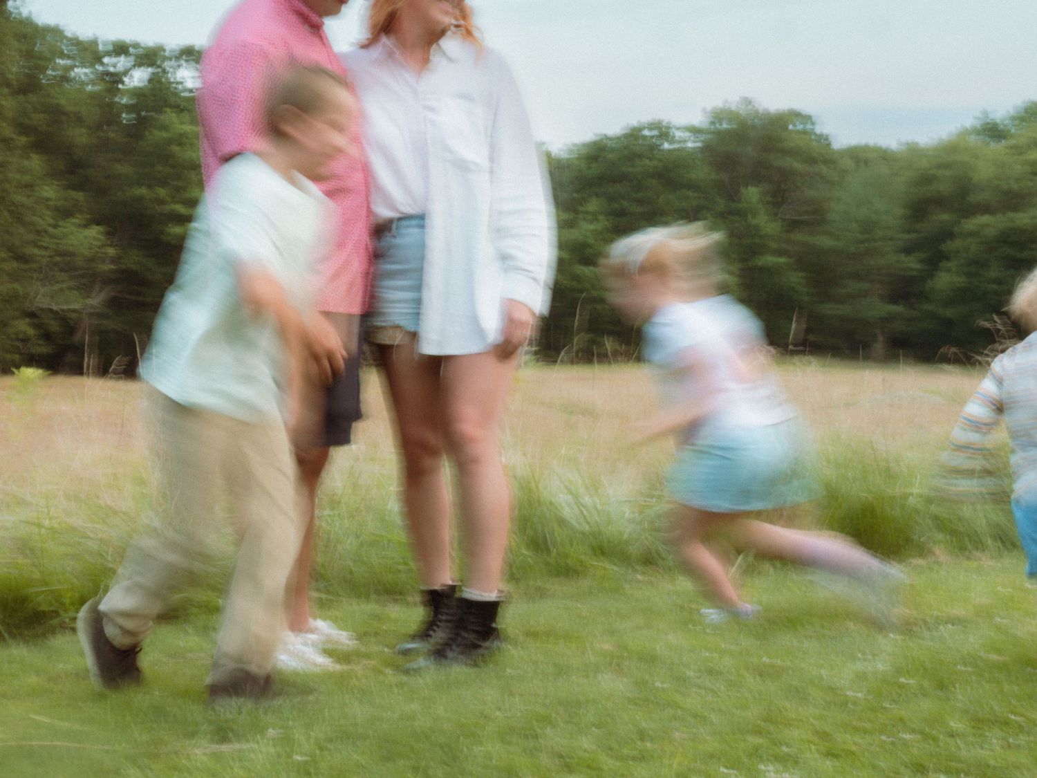 Family standing together in a meadow with children running around them.