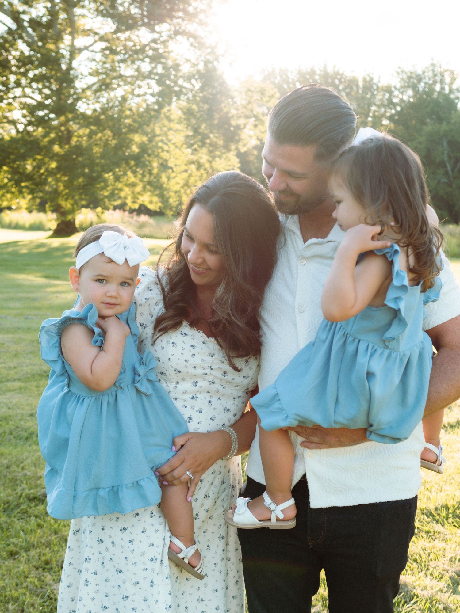 Happy family of four with two young daughters in matching blue dresses outdoors.