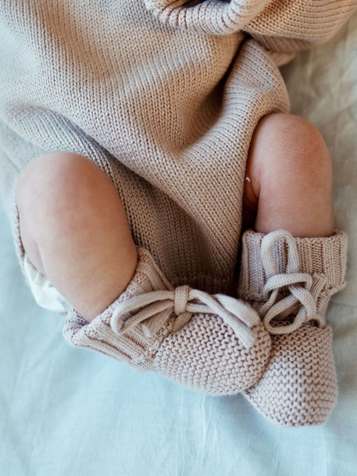 Close-up of baby feet in knit booties with lace-up ties, wearing a beige knit romper.