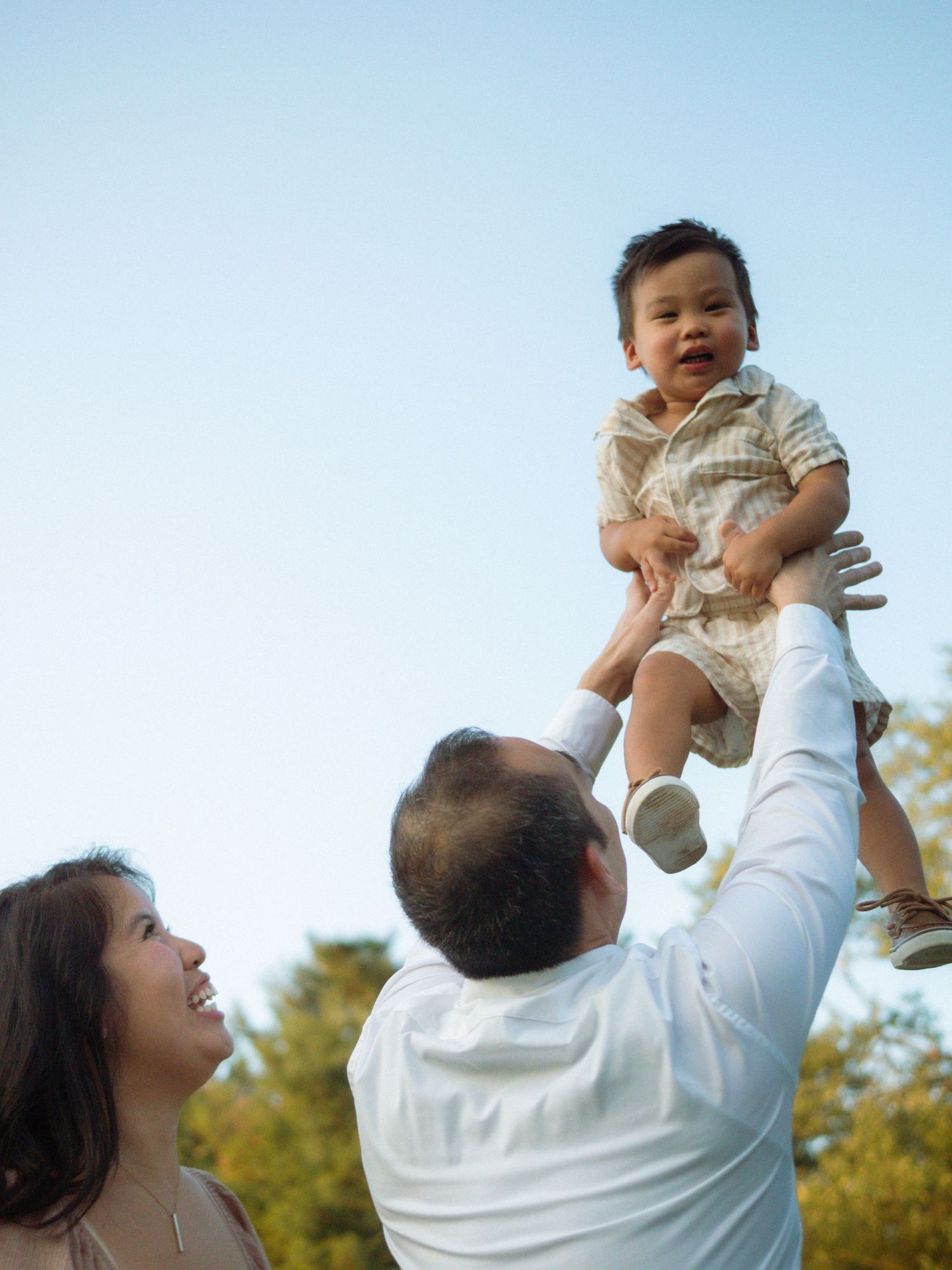 Joyful parents tossing smiling baby in the air against a blue sky.