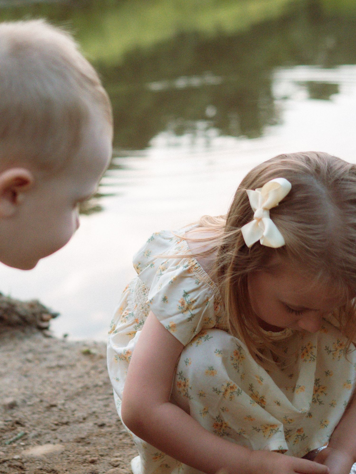 Two young children play together in the sand near a calm reflective pond.
