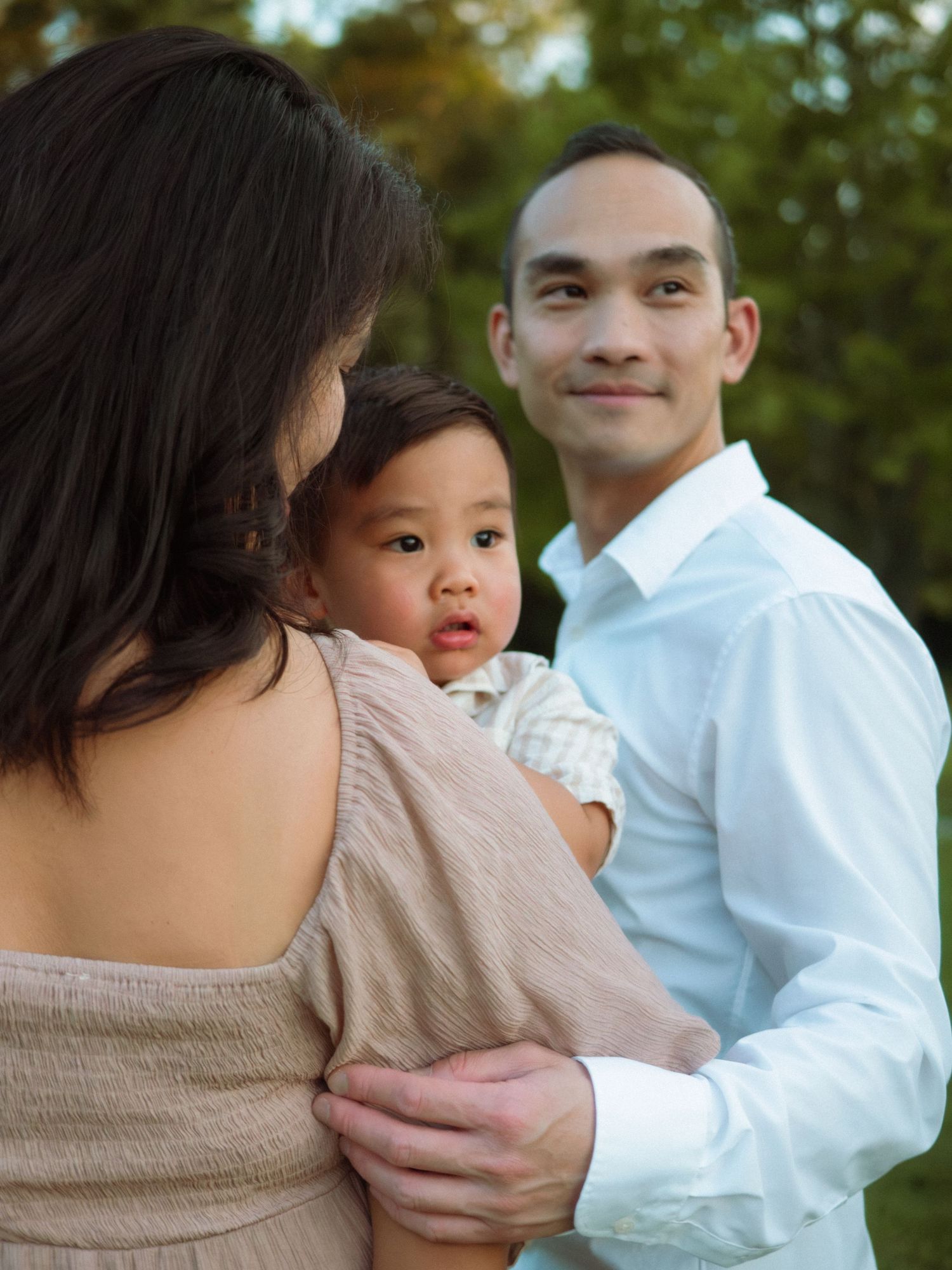 Asian parents tenderly hold their baby outdoors in warm golden light.