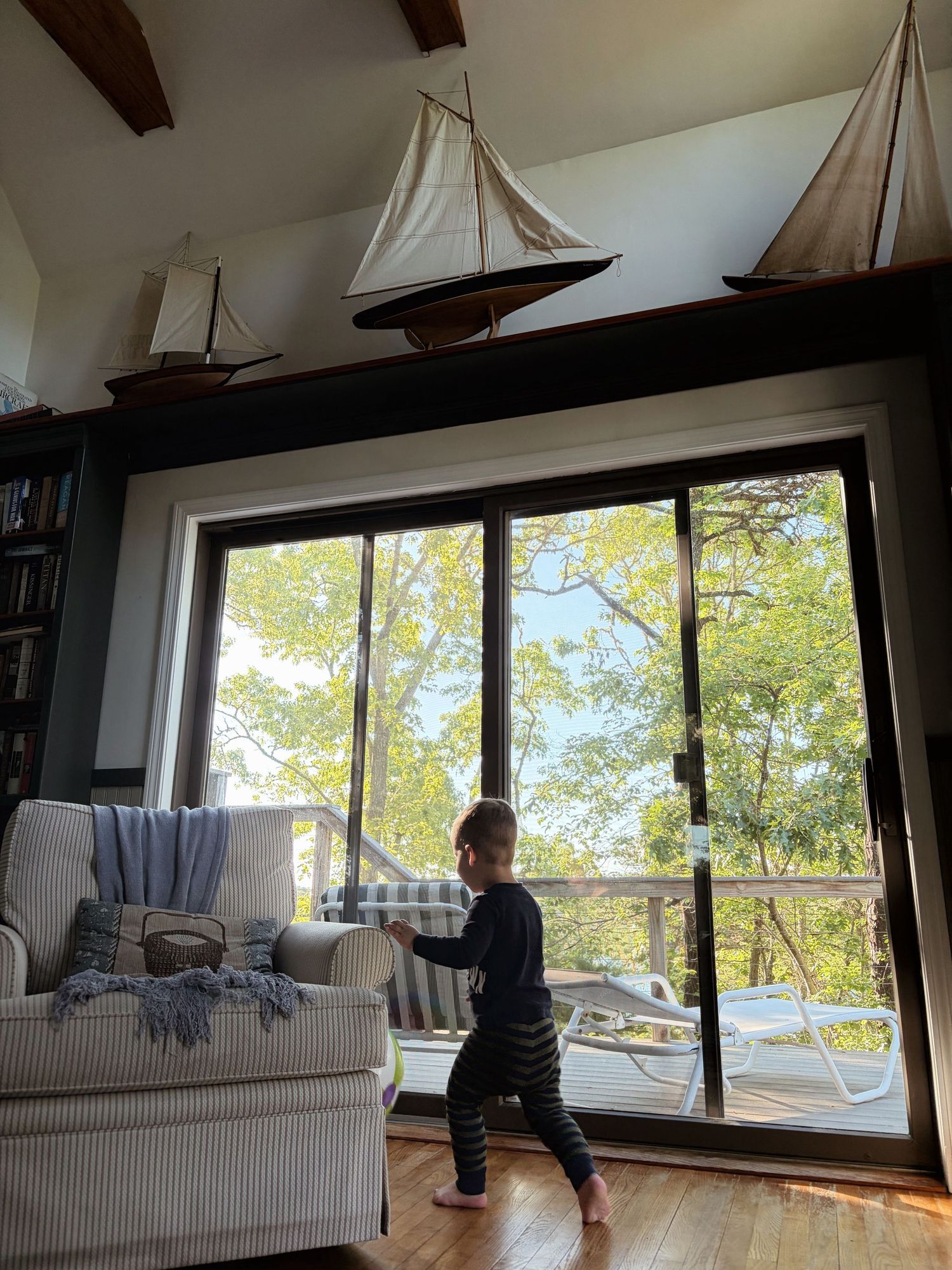 Young toddler walks through stylish living room with large window and decorative sailboats.