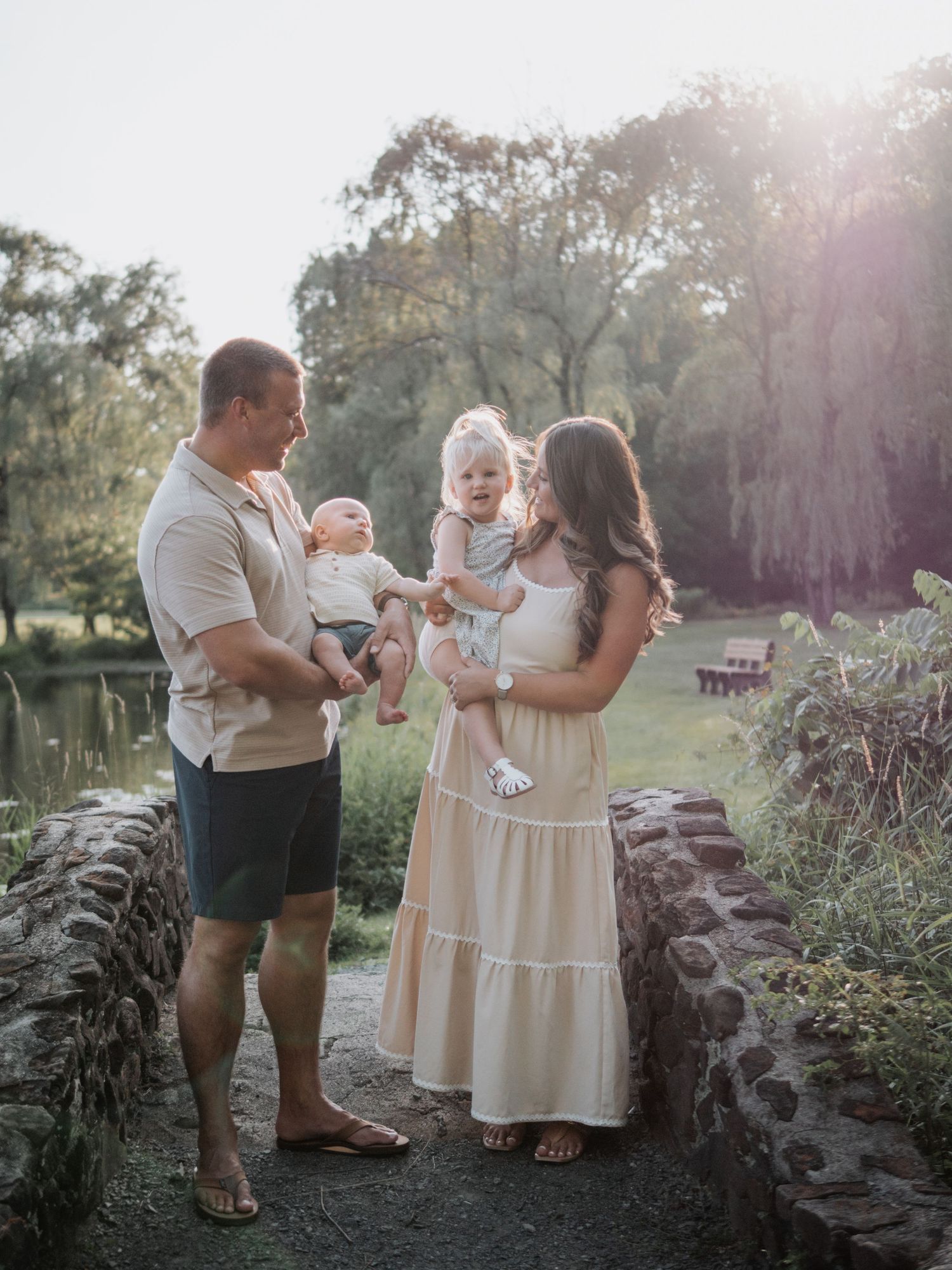 Family of four with two babies enjoying a golden hour moment in a lush park setting.