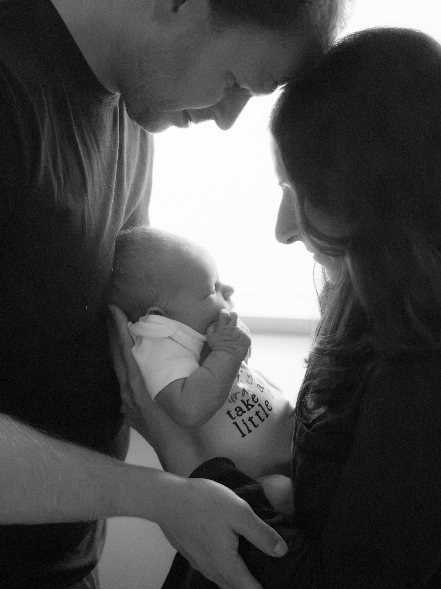 Black and white photo of new parents lovingly gazing at their newborn baby.