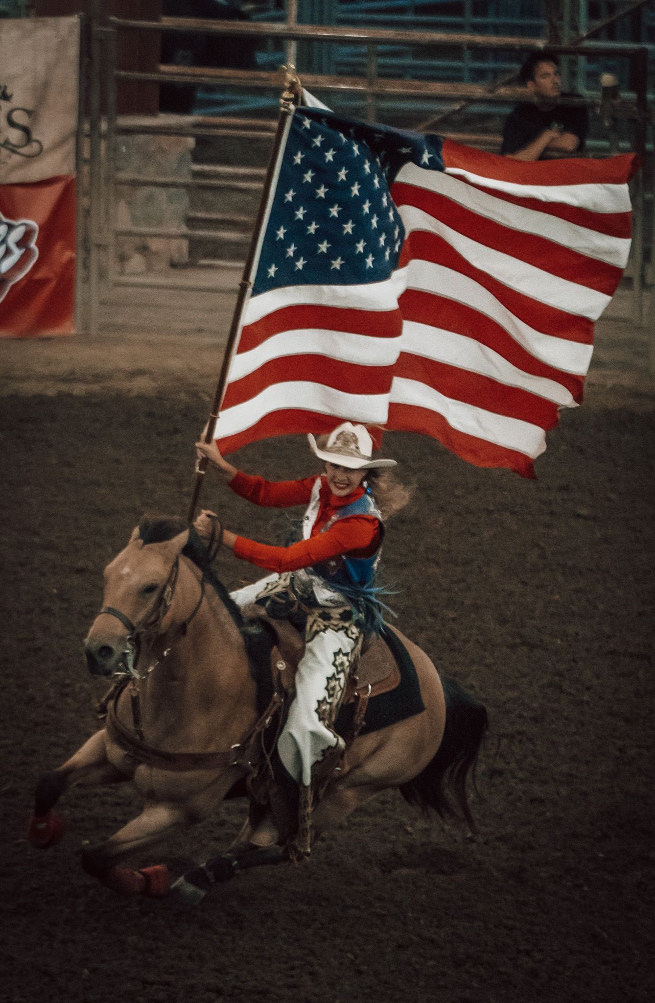Rodeo rider carrying a large American flag on horseback during a patriotic arena ceremony