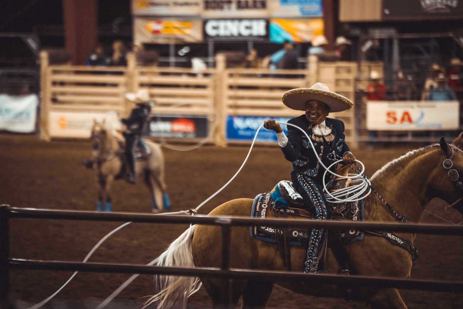 Rodeo cowboy on horseback swinging a lasso inside a Western arena