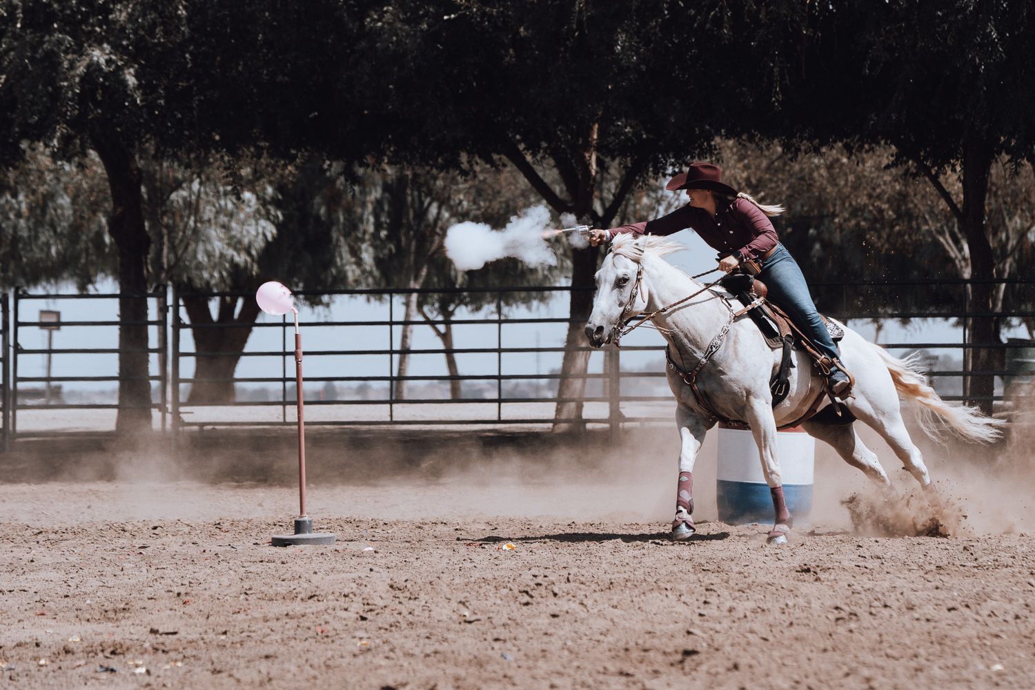 Cowboy mounted shooting competitor racing on horseback around a course marker in a cloud of dust