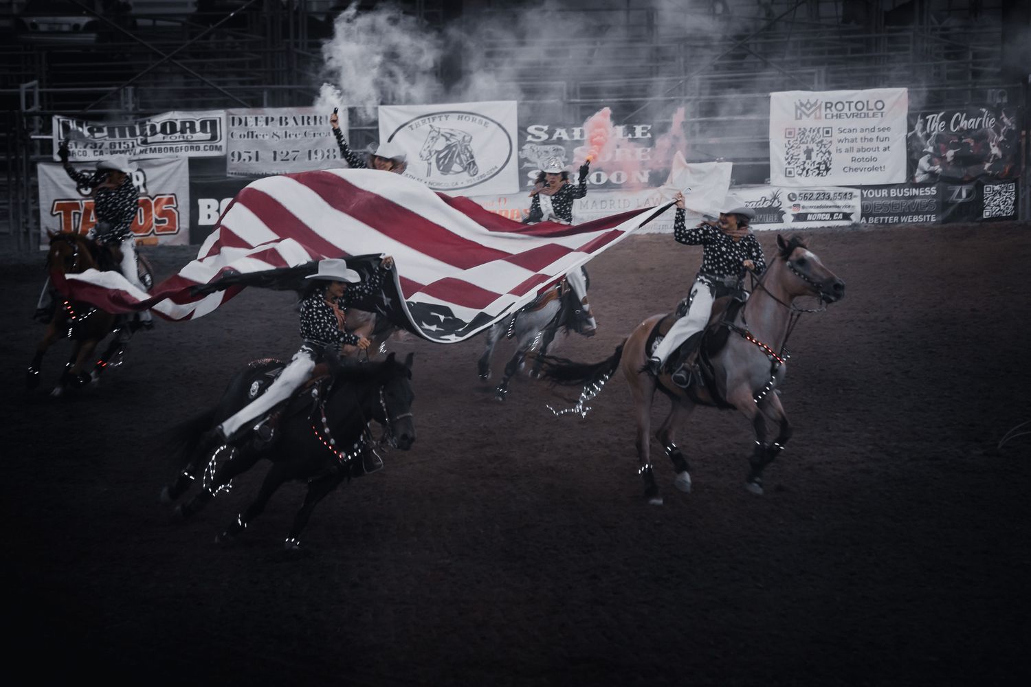 Rodeo riders carrying a large American flag on horseback during an arena ceremony