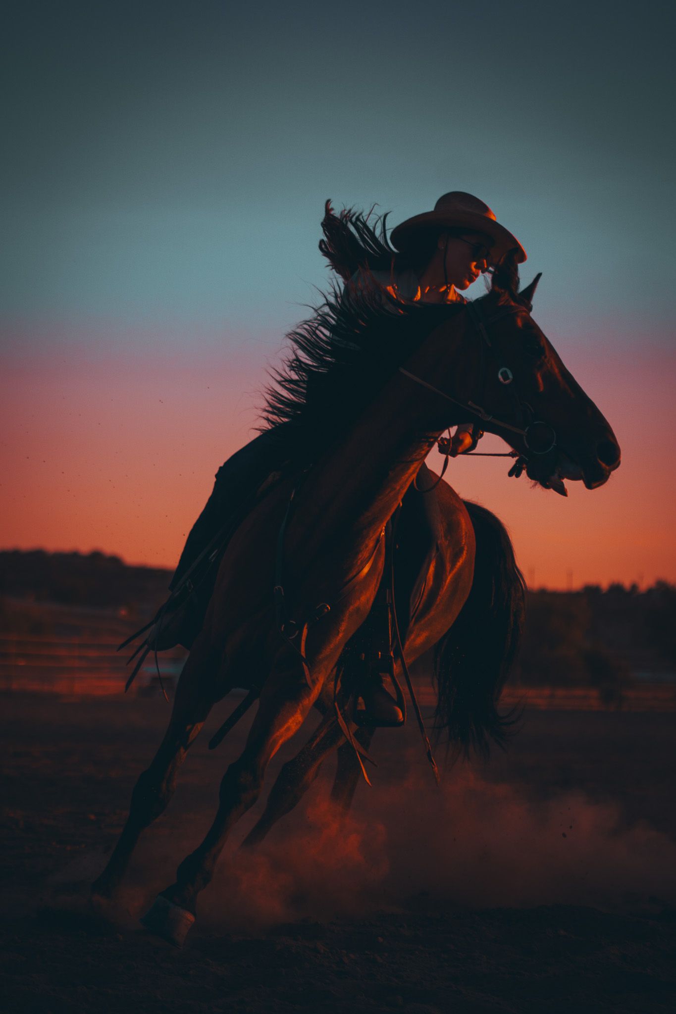 Western rider galloping on horseback through dust at sunset