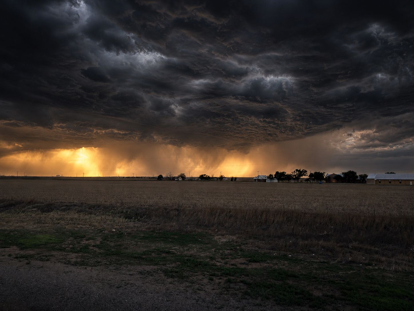 A dark shelf cloud and distant rain sweep across open farmland near Amarillo at sunset.