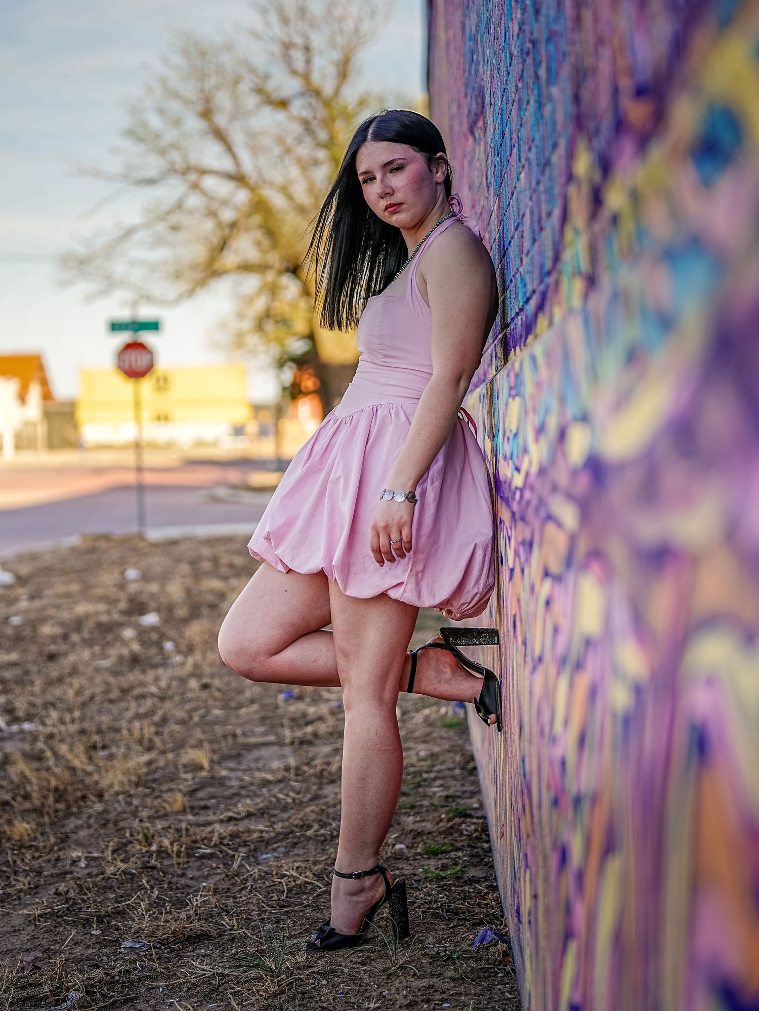 Amarillo senior portrait of a young woman in a pink dress posed beside a colorful painted mural