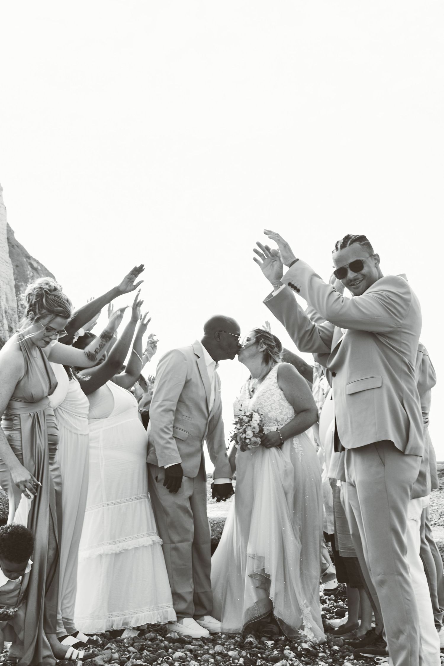 Photo de mariage en noir et blanc, mariés et invités qui célèbrent en levant les bras