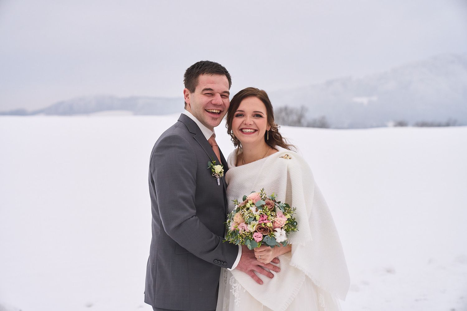 Mariés souriants dans un paysage enneigé, bouquet de fleurs à la main, mariage d'hiver