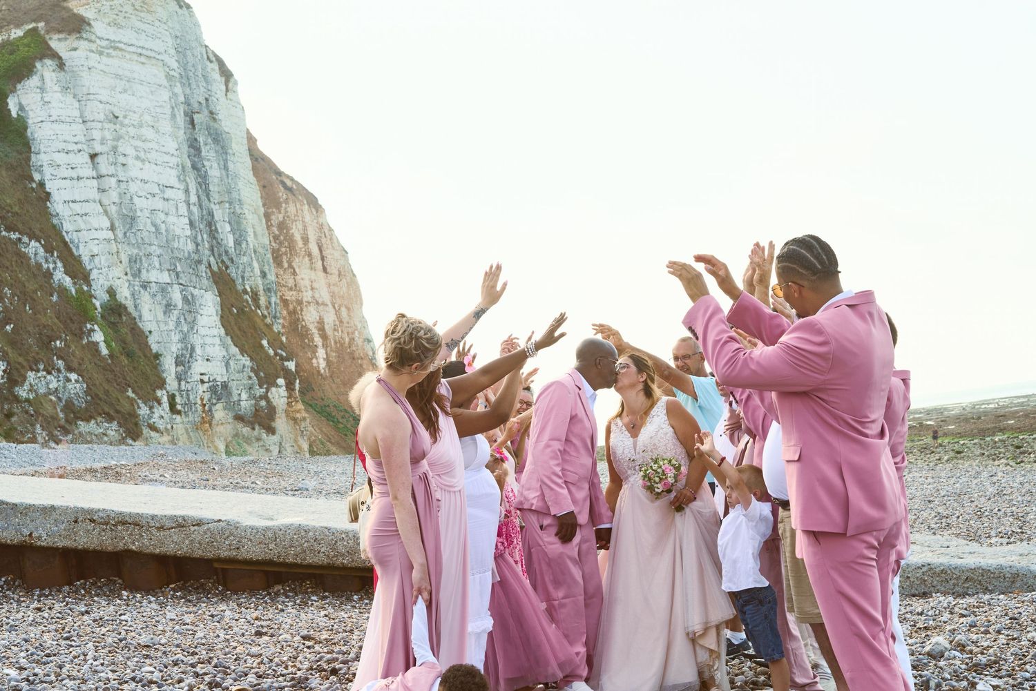 Mariés et invités en rose sur une plage de galets au pied des falaises en Normandie
