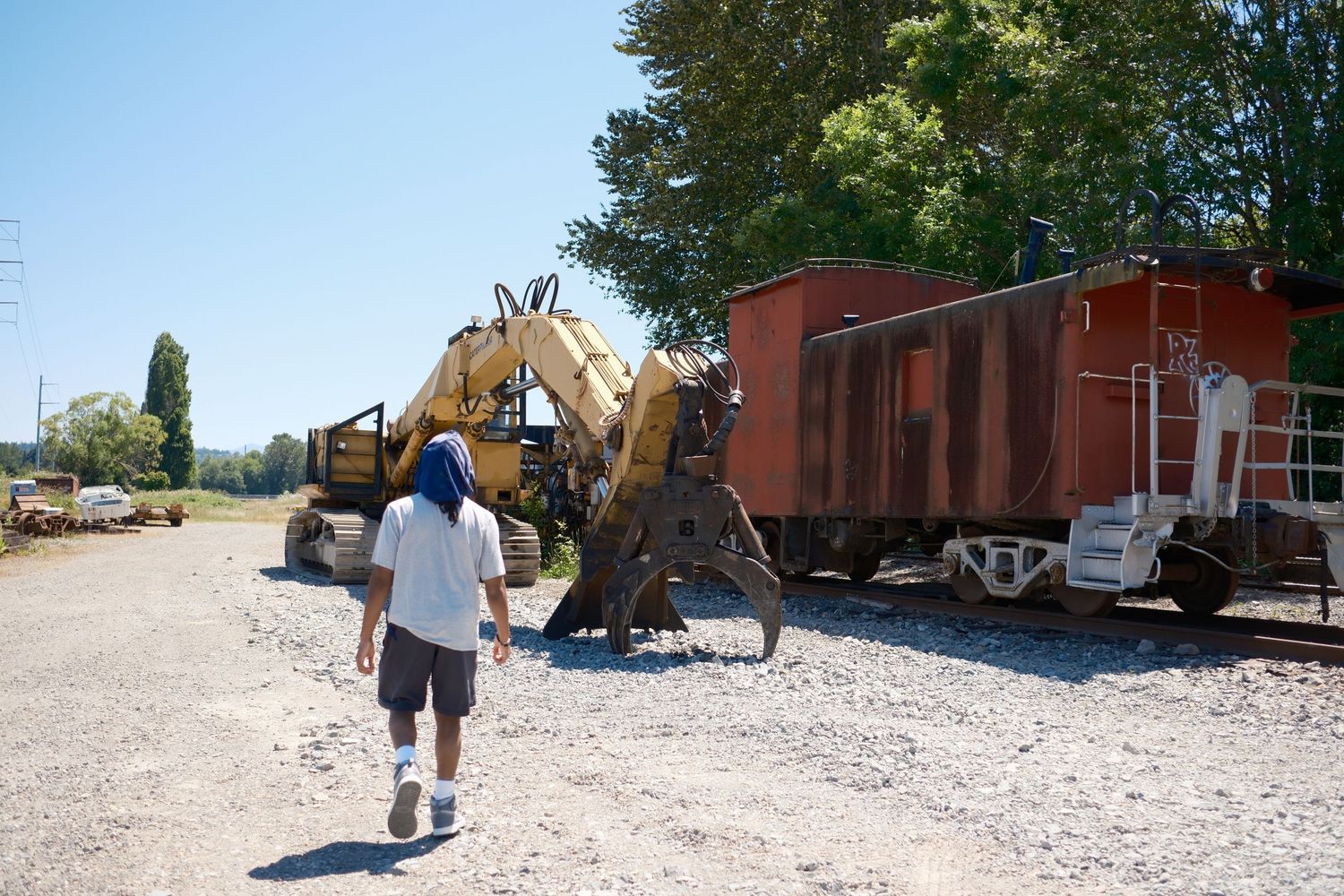 Portrait of a person walk toward a abandoned train yard and a construction vehicle