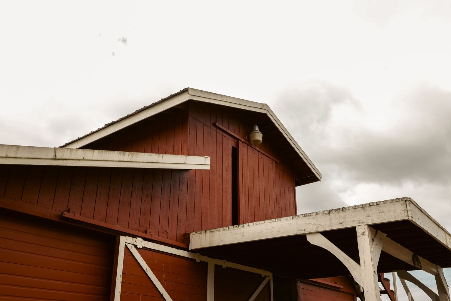 Close-up architectural photograph of a red barn beneath an overcast sky.