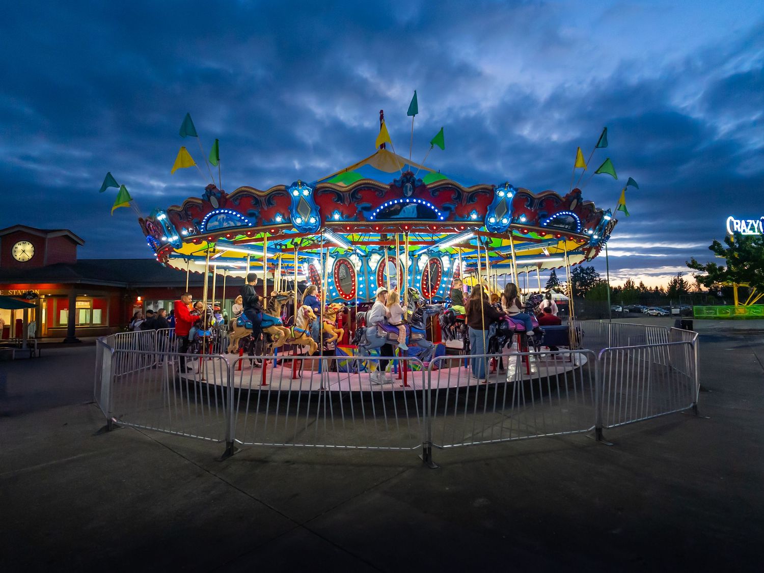 Colorful carnival ride illuminated at dusk beneath a dramatic blue sky.