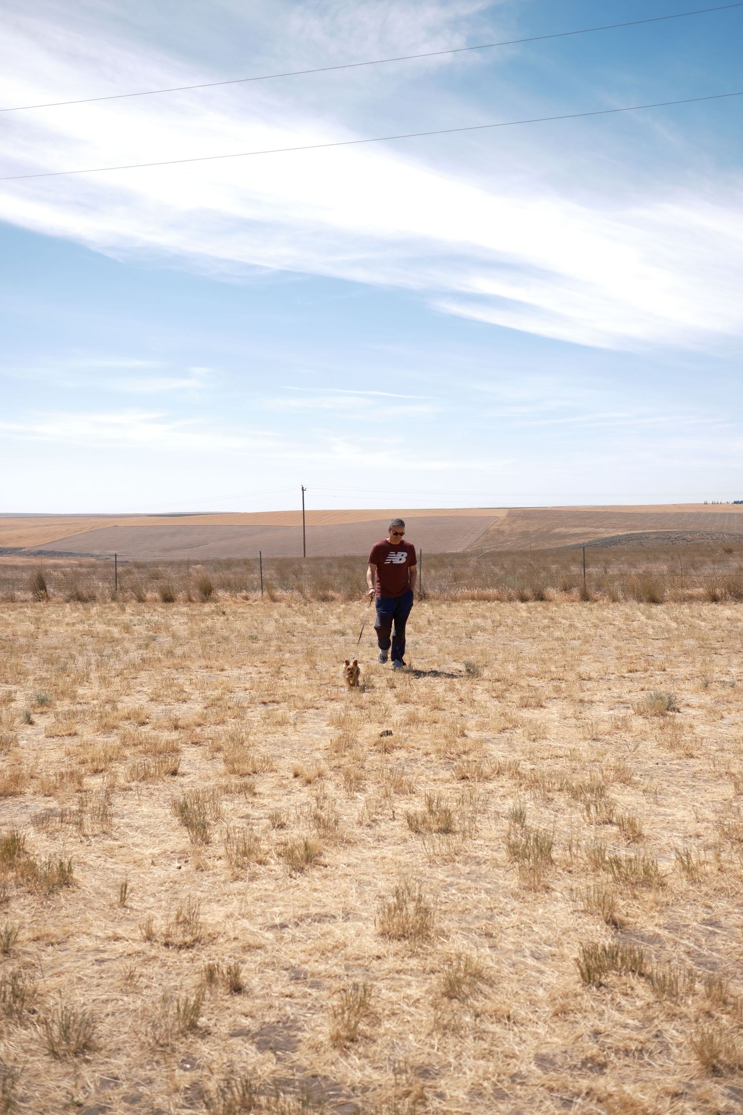 Portrait of a person standing in an open field beneath a blue sky.
