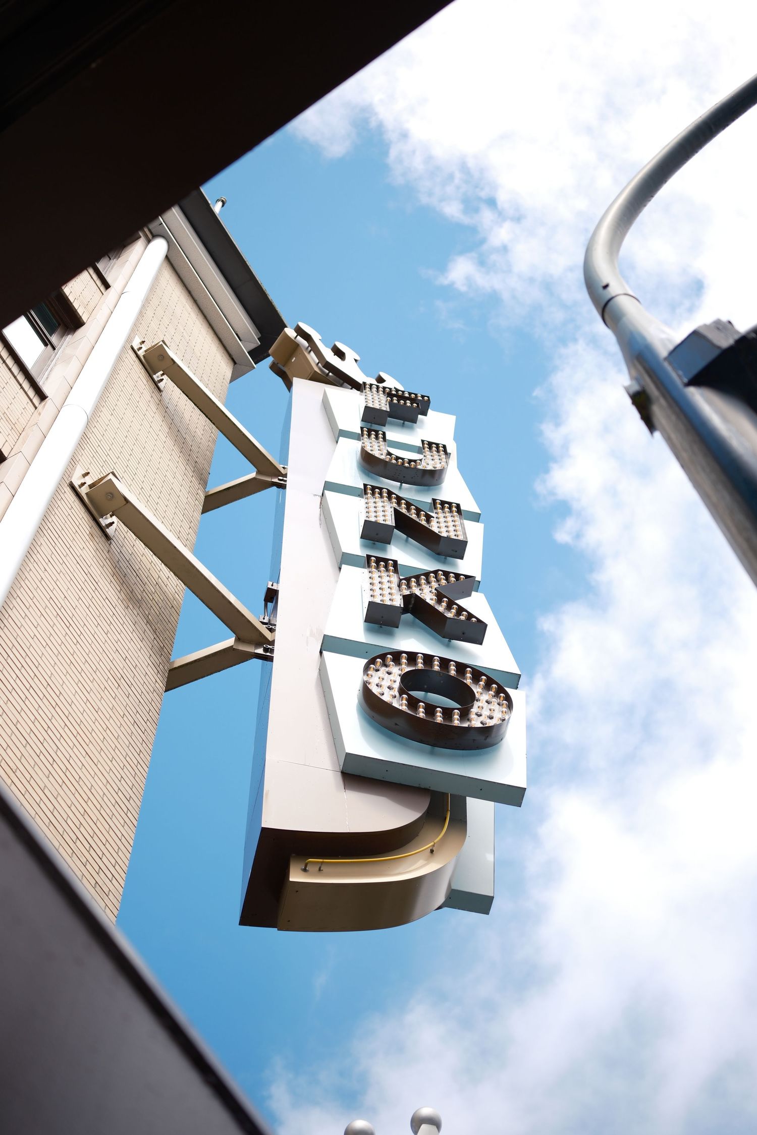 Upward angle of a store sign against a bright blue sky with clouds arcing around