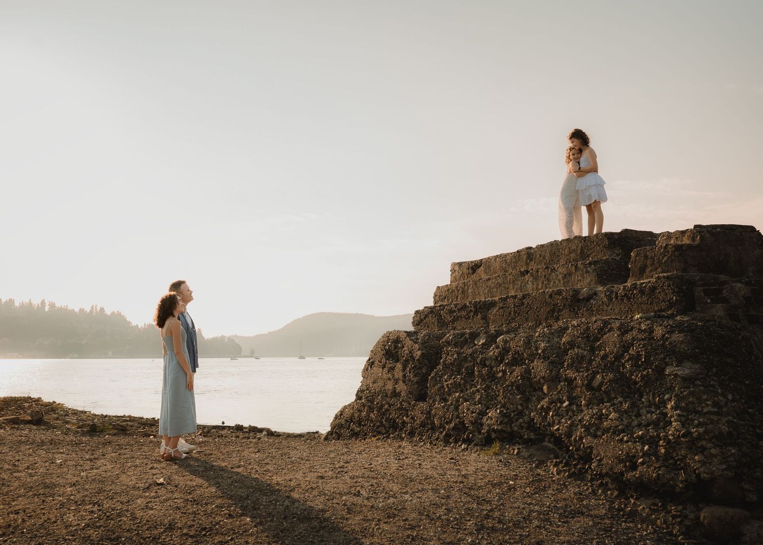 A person in a white dress stands on a rocky cliff overlooking a misty coastal landscape at sunset.