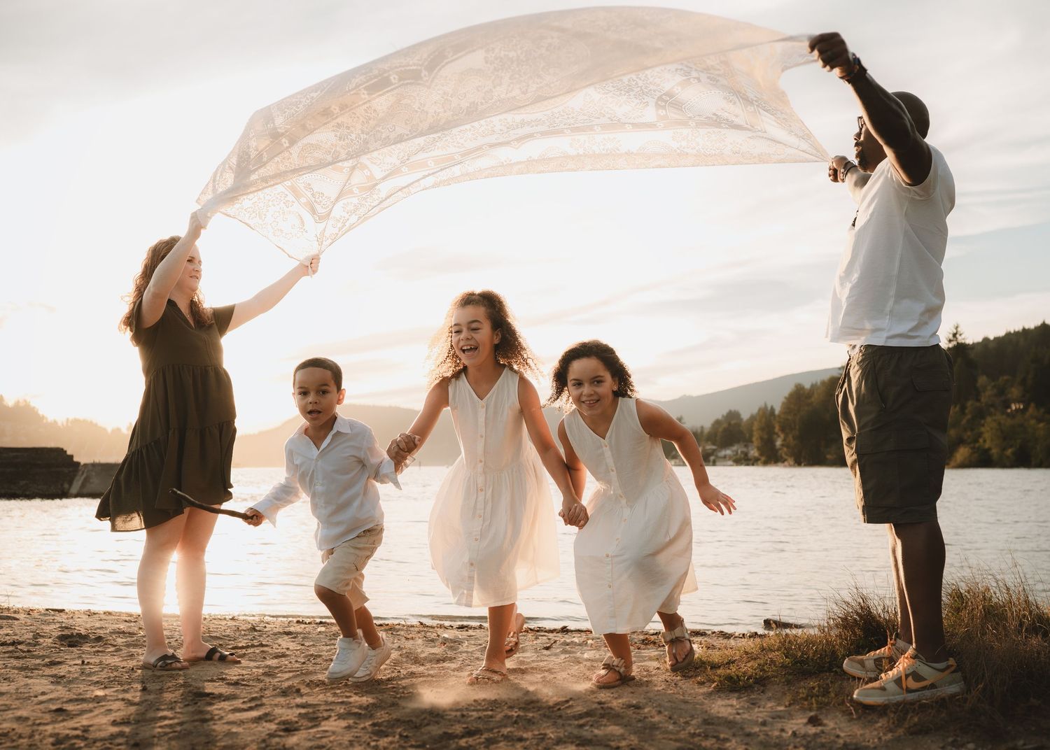 Wedding couple dances playfully on a scenic beach at sunset with flowing white dress and veil in the wind.