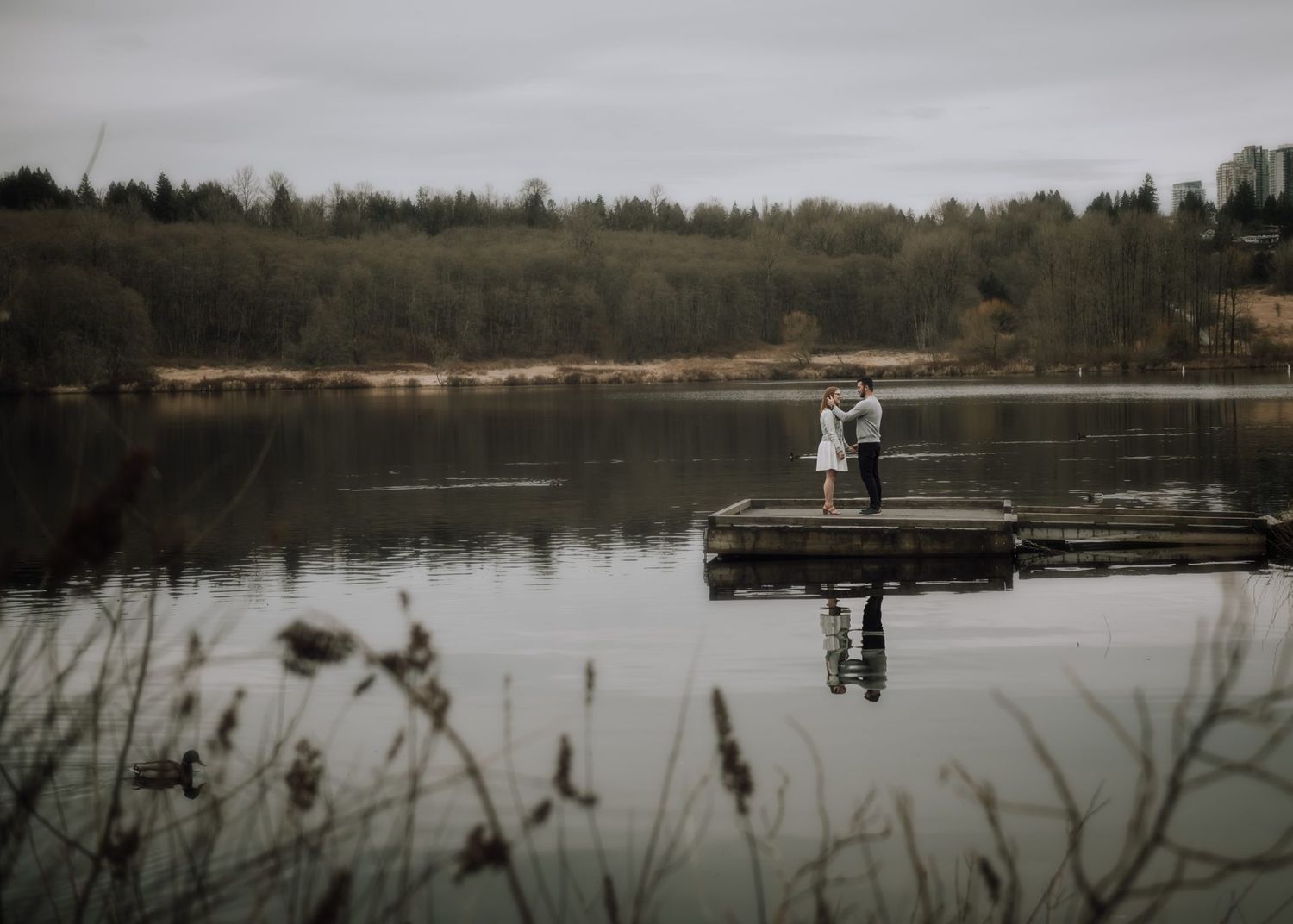 Couple standing on wooden dock over misty lake for moody wedding photo.