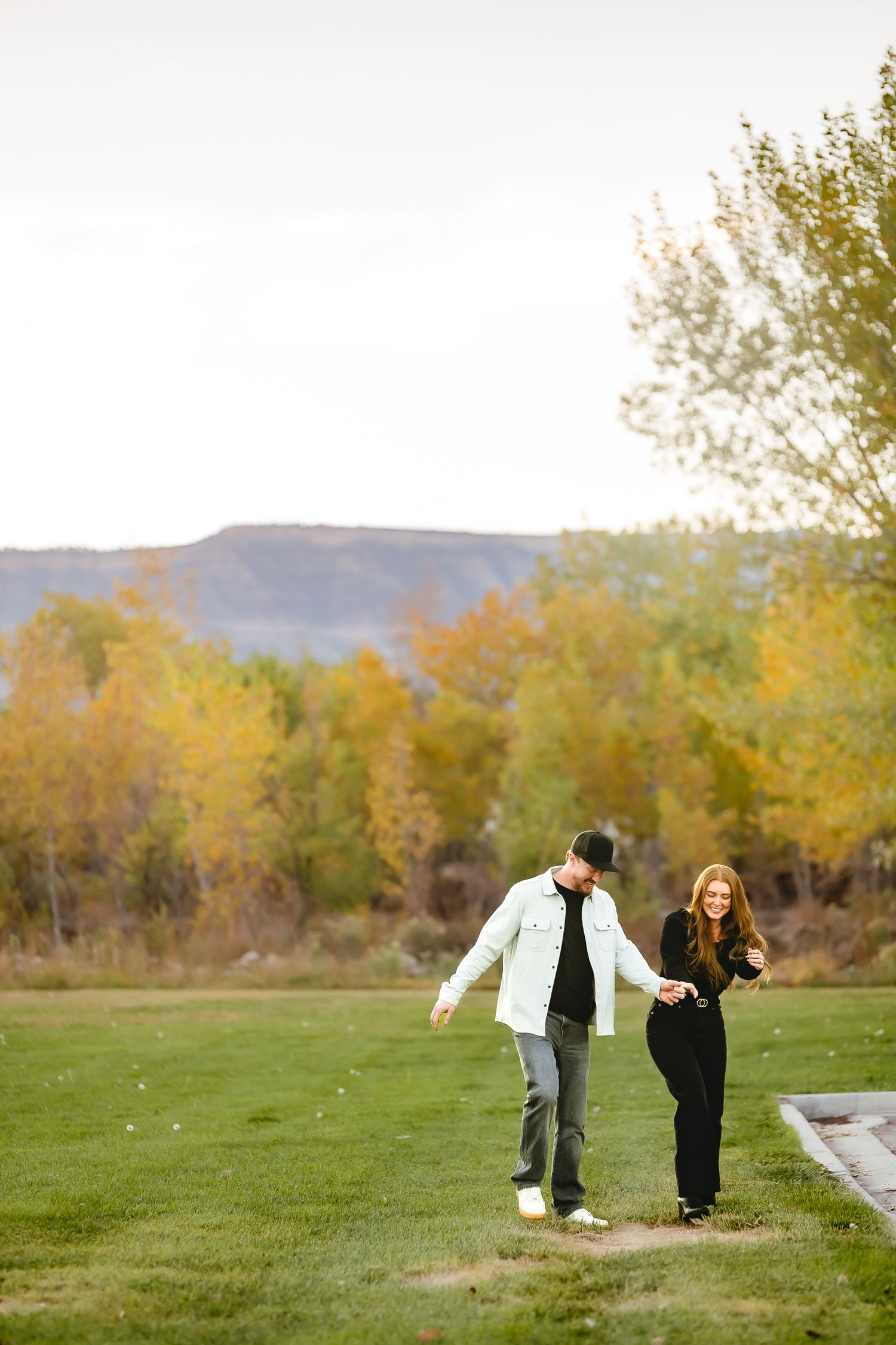 Playful interaction between adults on a grassy field with autumn trees in the background.