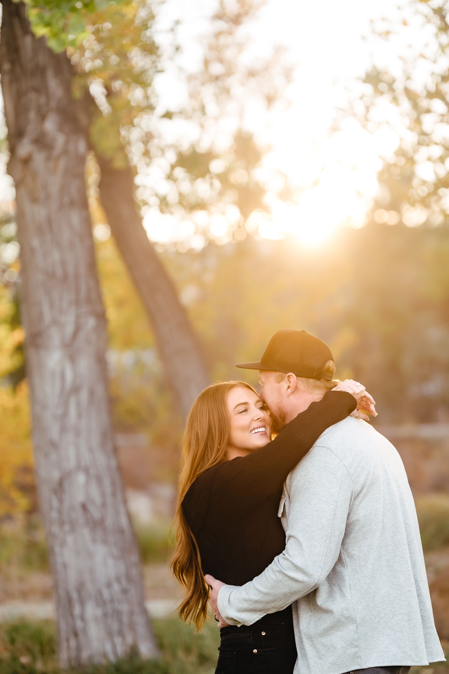 Romantic couple sharing intimate moments at sunset among trees in a park.