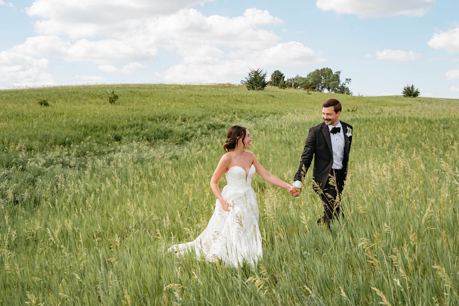 Couple walking through a serene green meadow in formal wedding attire.