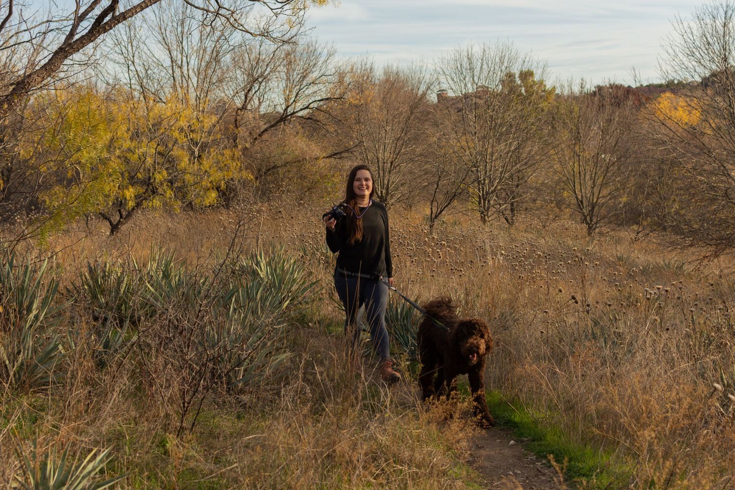A young woman and her dog walk through a field during a winter creative portrait session in Panther City, Fort Worth, TX.