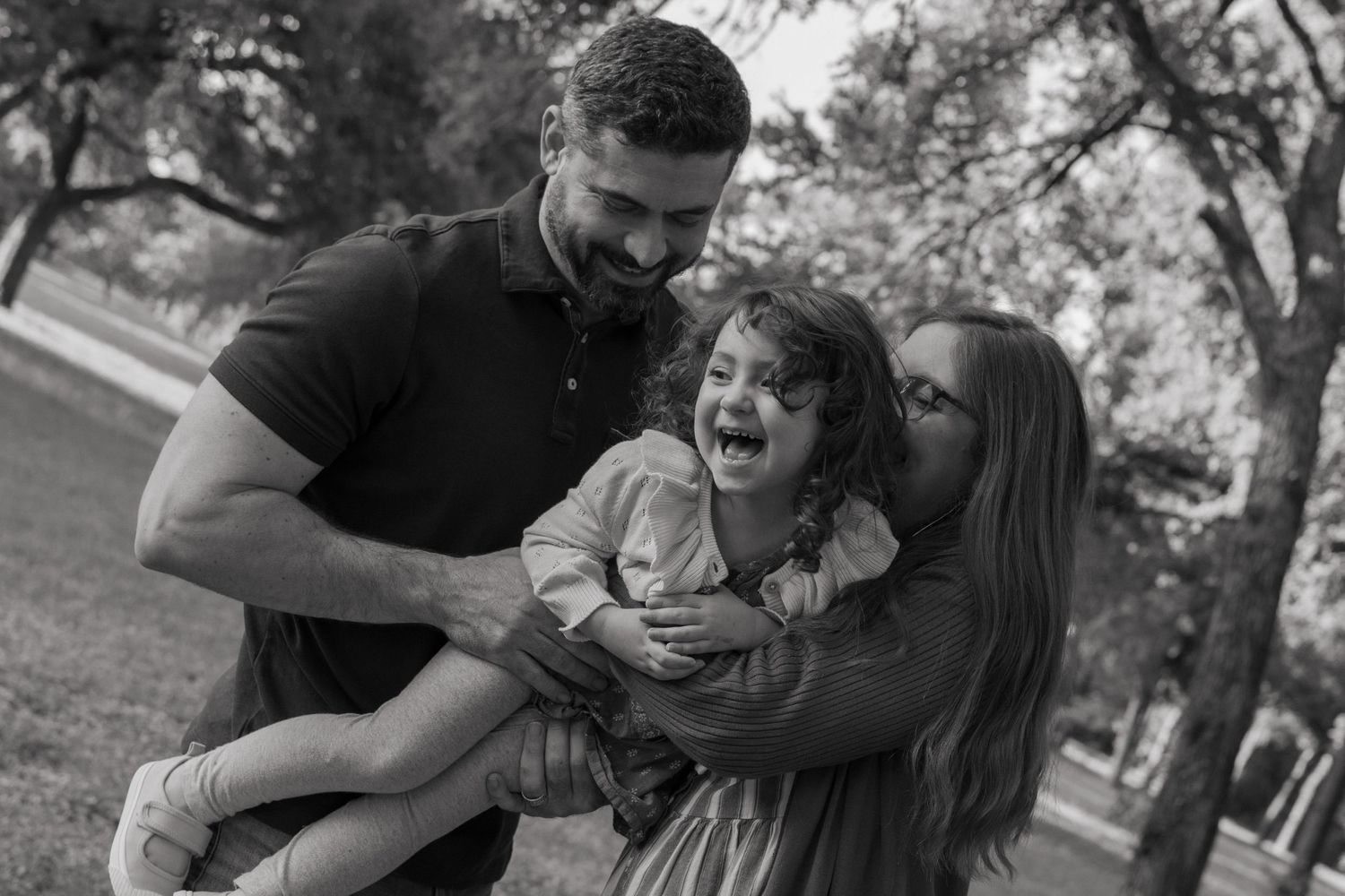 A black-&-white photo of a mom and dad holding and tickling their youngest child during a north Texas family photoshoot in the spring.