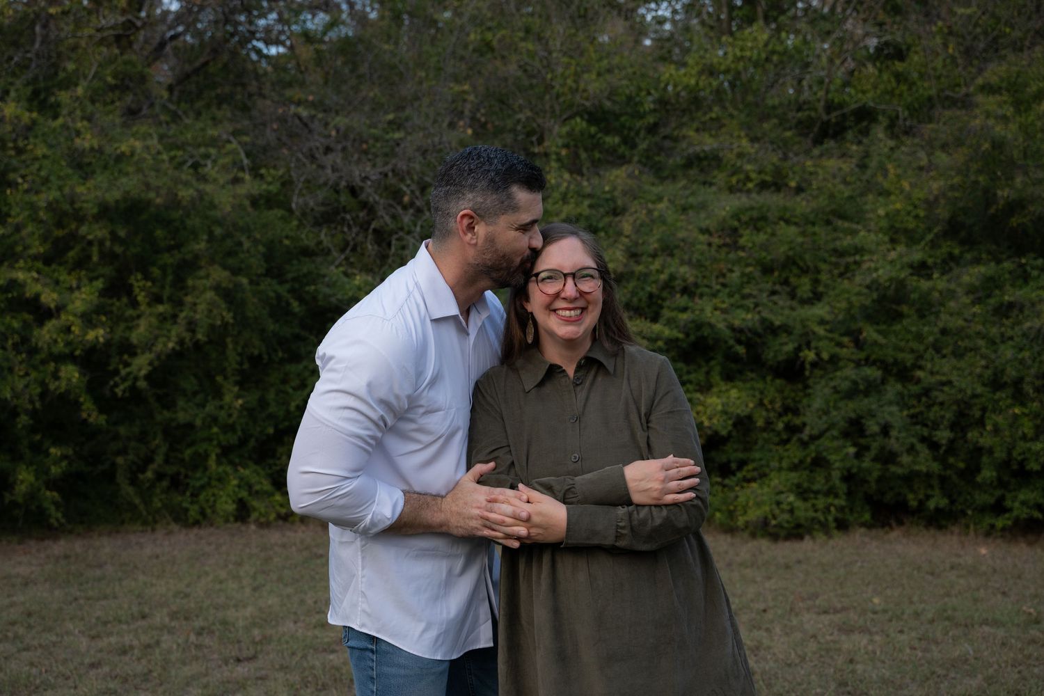 A husband kisses his wife's head after saying something that made her laugh during a fall family portraits session in Fort Worth.