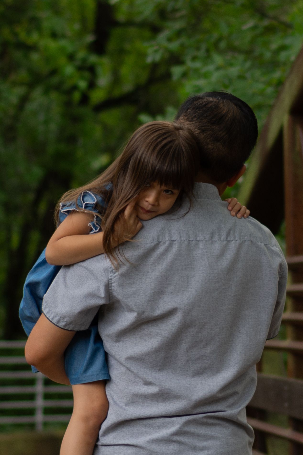 Father holds his young daughter in his arms during a family session. She looks over his shoulder, tired, as he walks away from photographer.