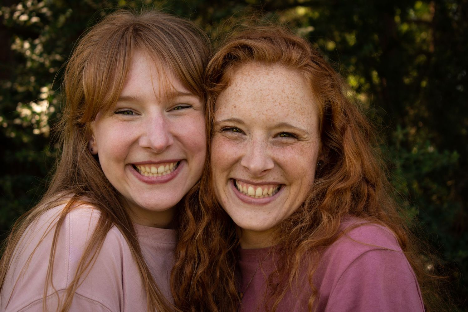 A couple of red-headed sisters pose cheek-to-cheek while smiling at the camera during a roommate and sibling photoshoot in the spring in TX.