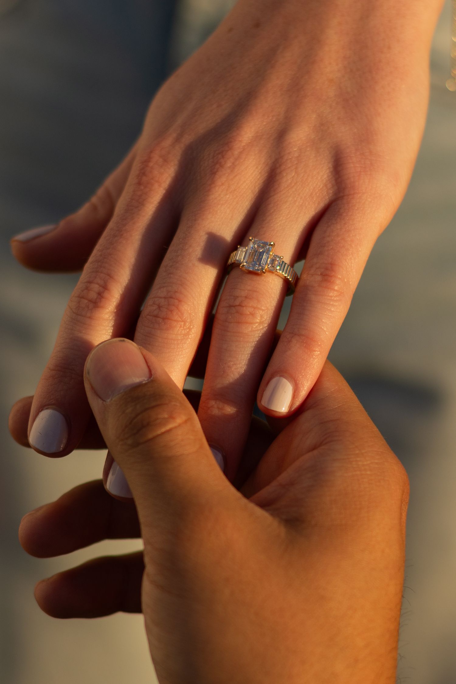 Close-up of a man's hand gently holding his fiancée's hand with her custom engagement ring made by Sovereign Jewelers in Fort Worth, TX.