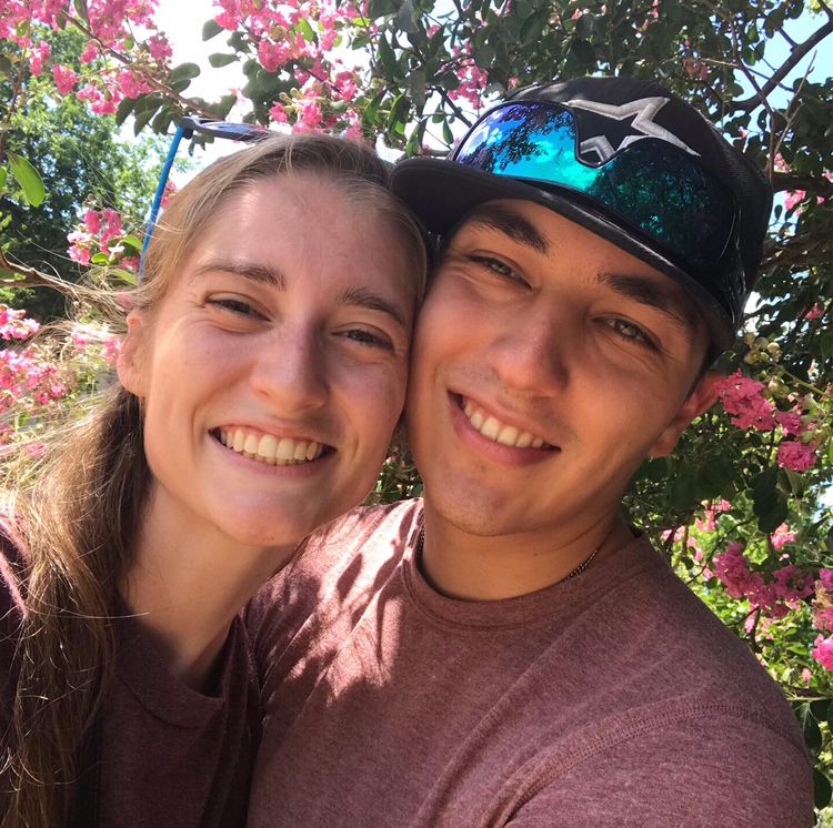 A selfie photo of Brooke and her husband smiling and standing in front of a blossoming pink crepe myrtle tree in spring in Texas.