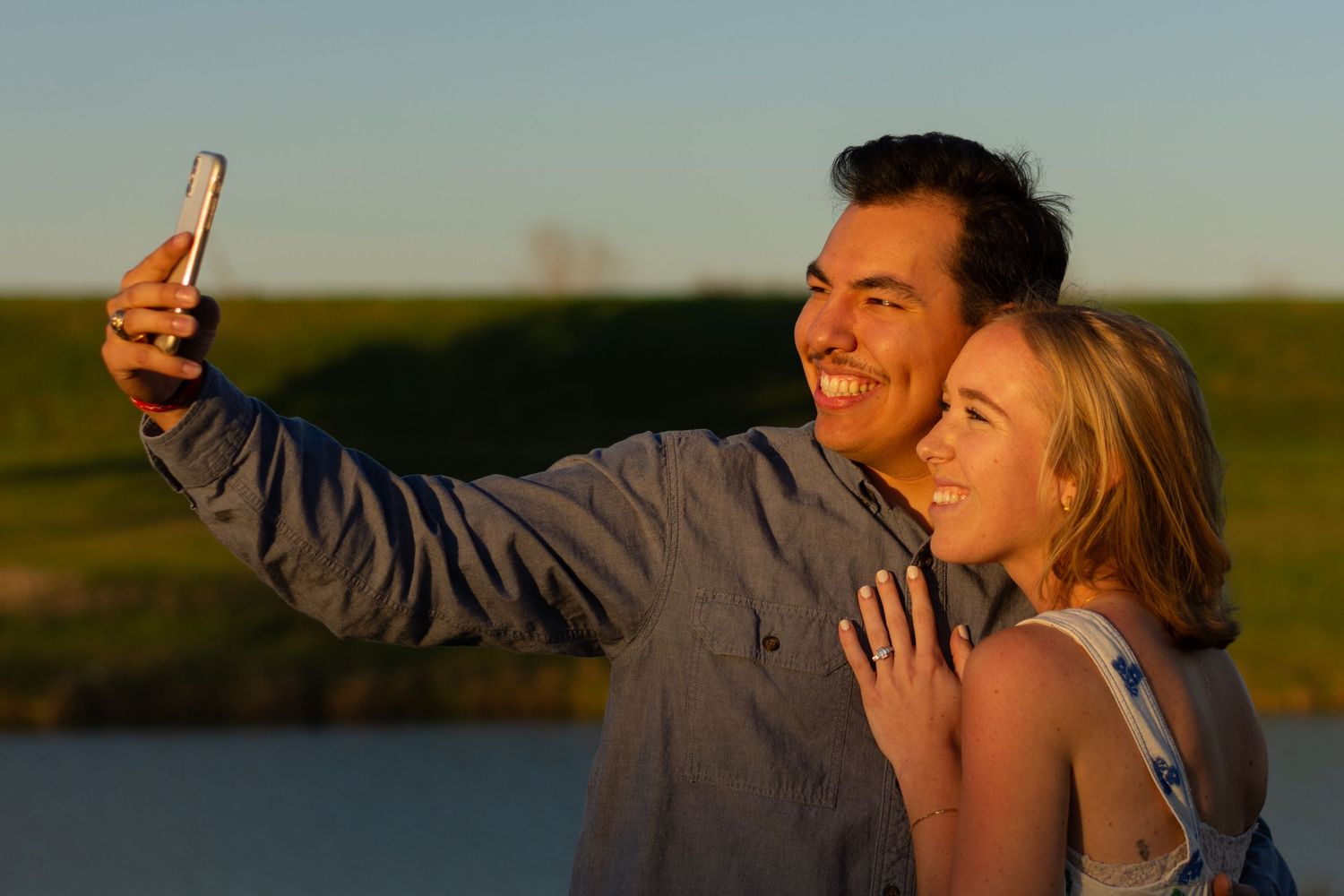 Candid at sunset of a newly engaged couple taking a selfie to send to their families to tell them to good news. Located at a Fort Worth park