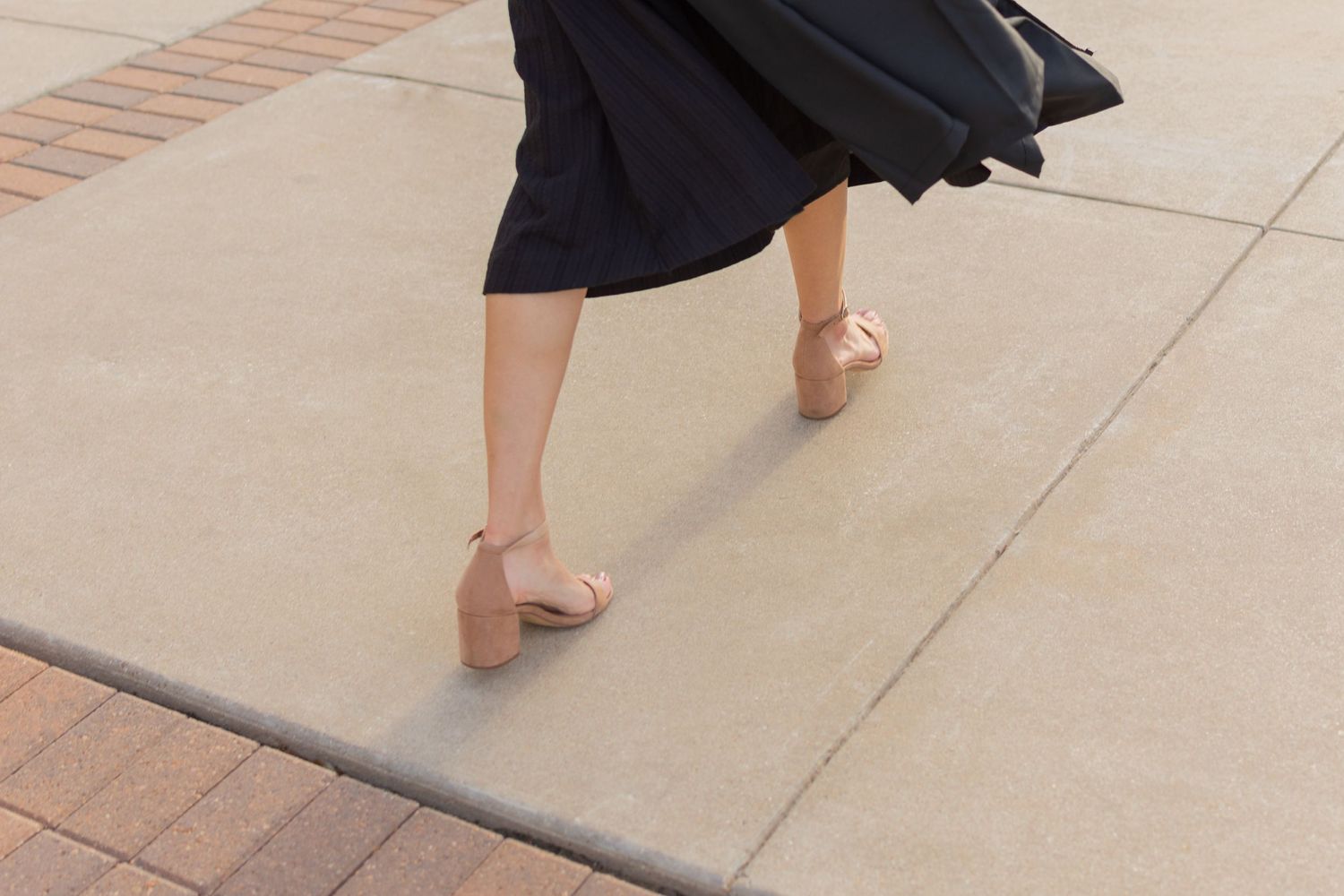 Downward candid photo of grad's nude heels and flowy black gown during an in-between moment snapped when walking to the next photo location.