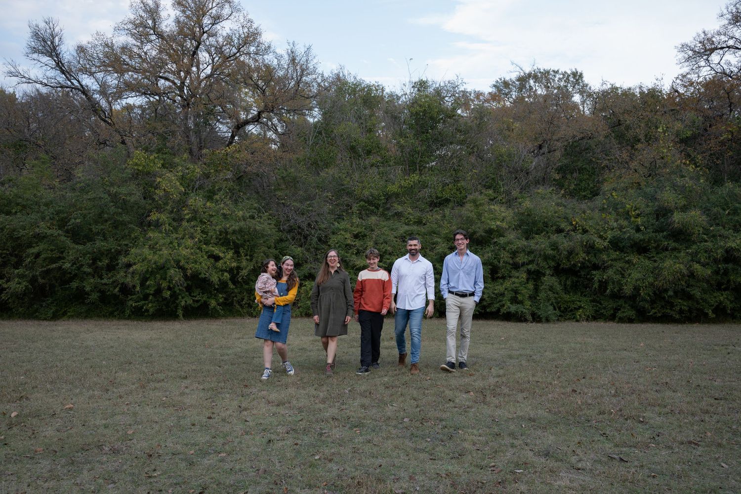 Zoomed-out photo of a Fort Worth family during a fall family session on a cloudy day in a park. They walk together toward the camera.