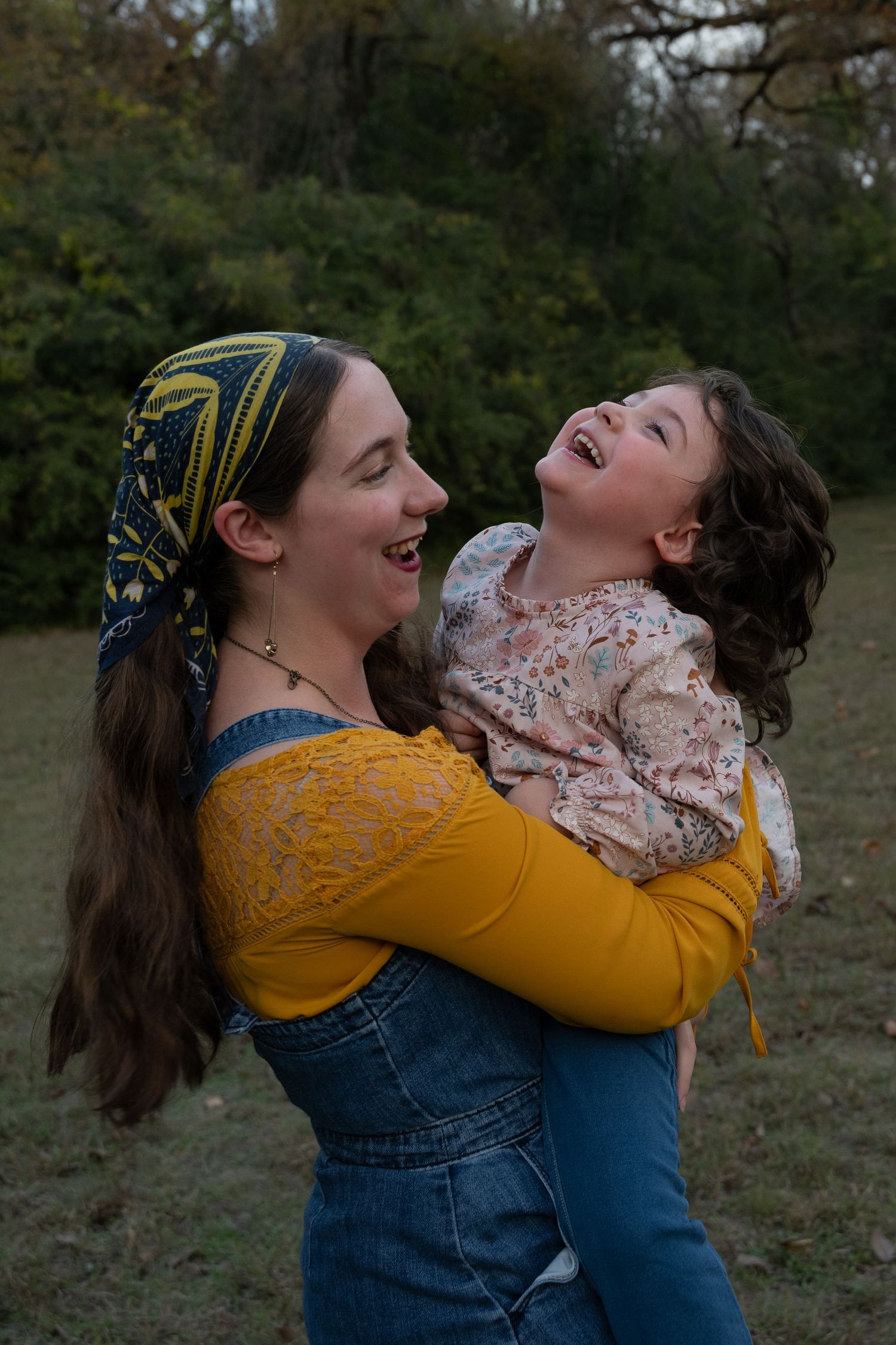 A toddler laughs, throwing her head back, as her older teen sister holds her and smiles during a Fort Worth fall family photoshoot session.