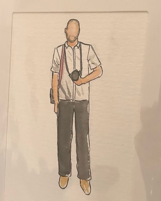 Fashion illustration of a man wearing a white shirt, dark trousers, tan shoes, and carrying a camera with a red strap.