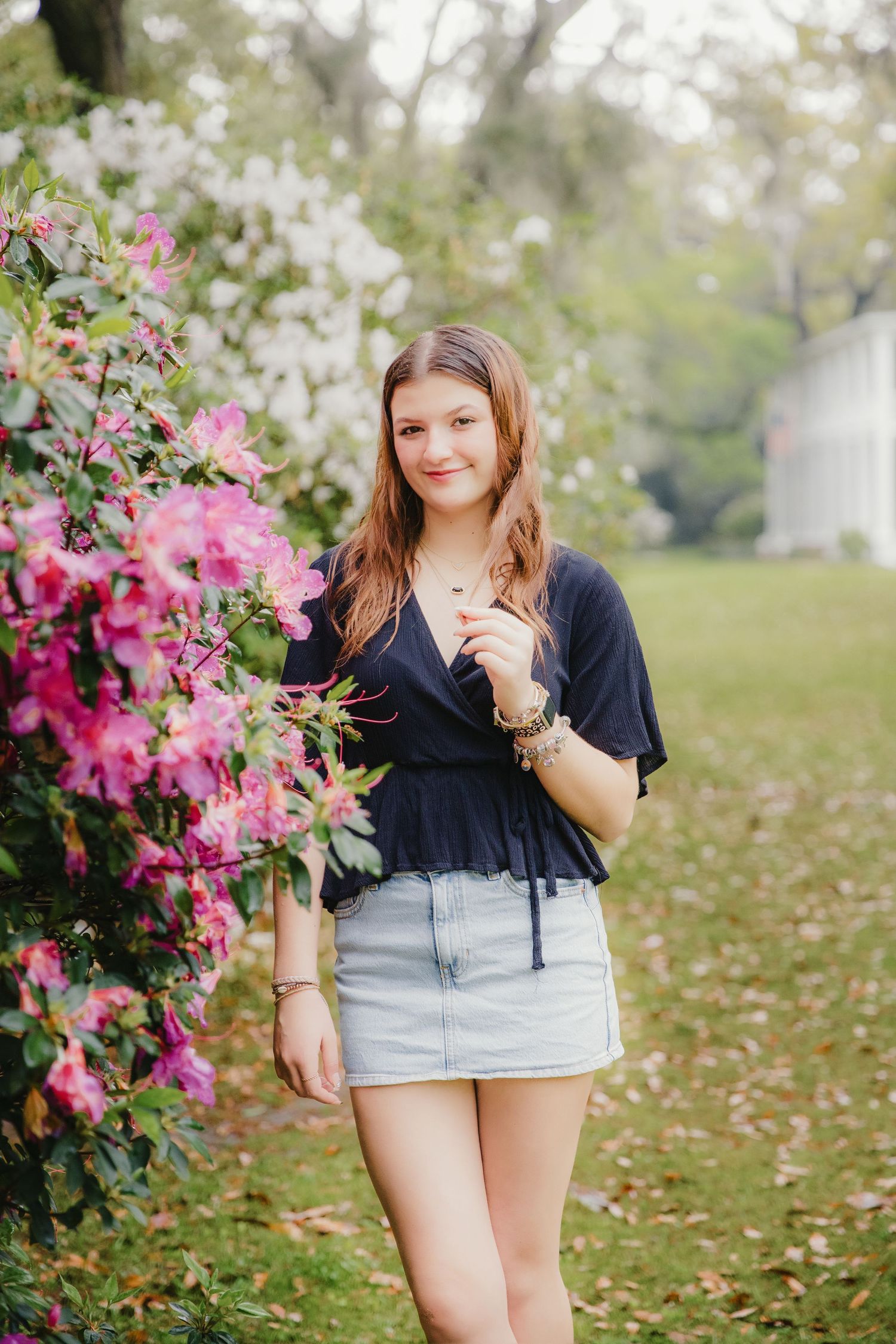Person in navy top and denim skirt standing next to blooming pink azalea bush.