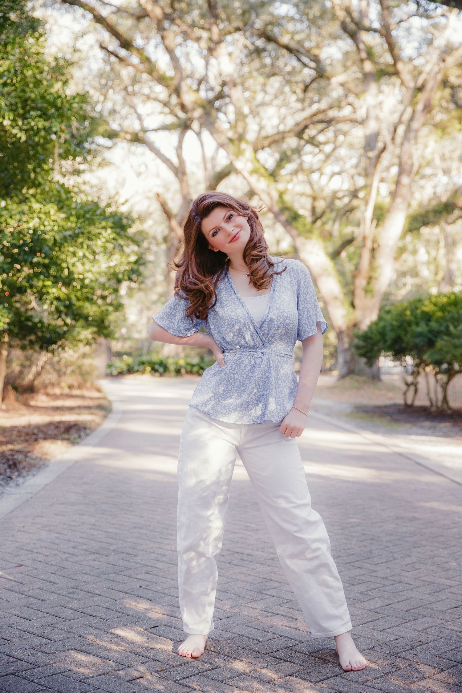 A springtime portrait in a floral top and white pants on a brick pathway.