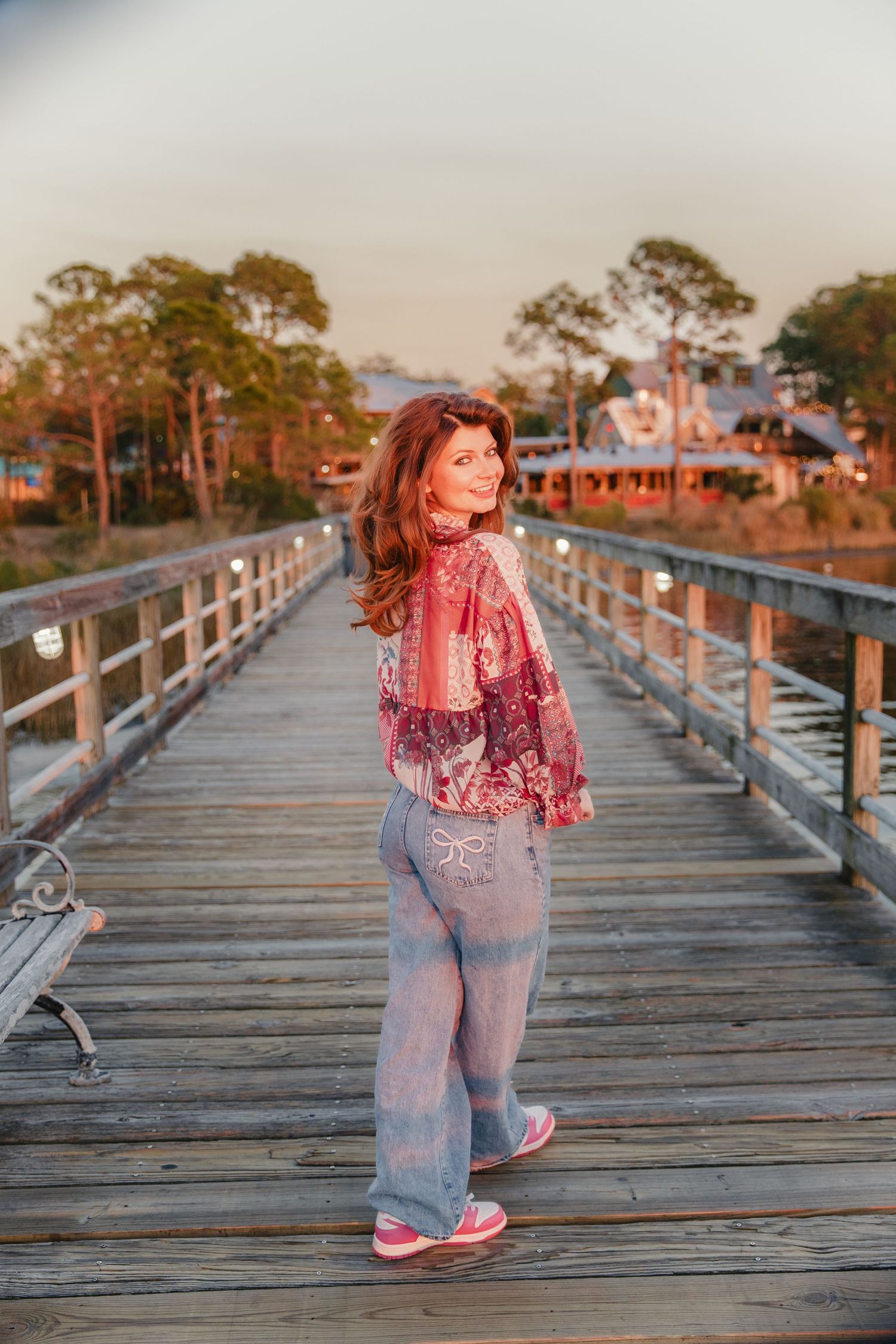 A sunset portrait on a wooden pier wearing a pink floral top and jeans.