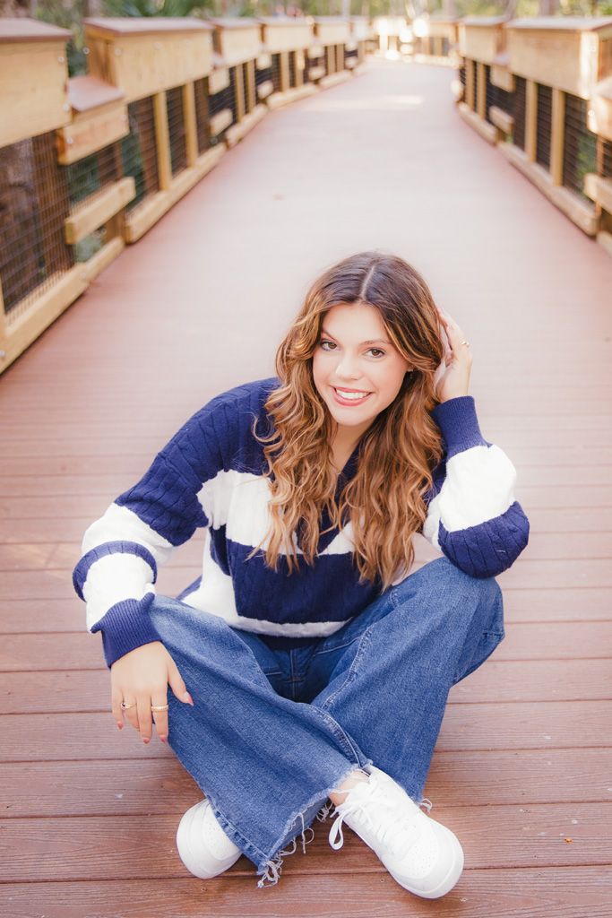 Person in blue denim jeans and white top sitting casually on wooden deck in warm sunlight.