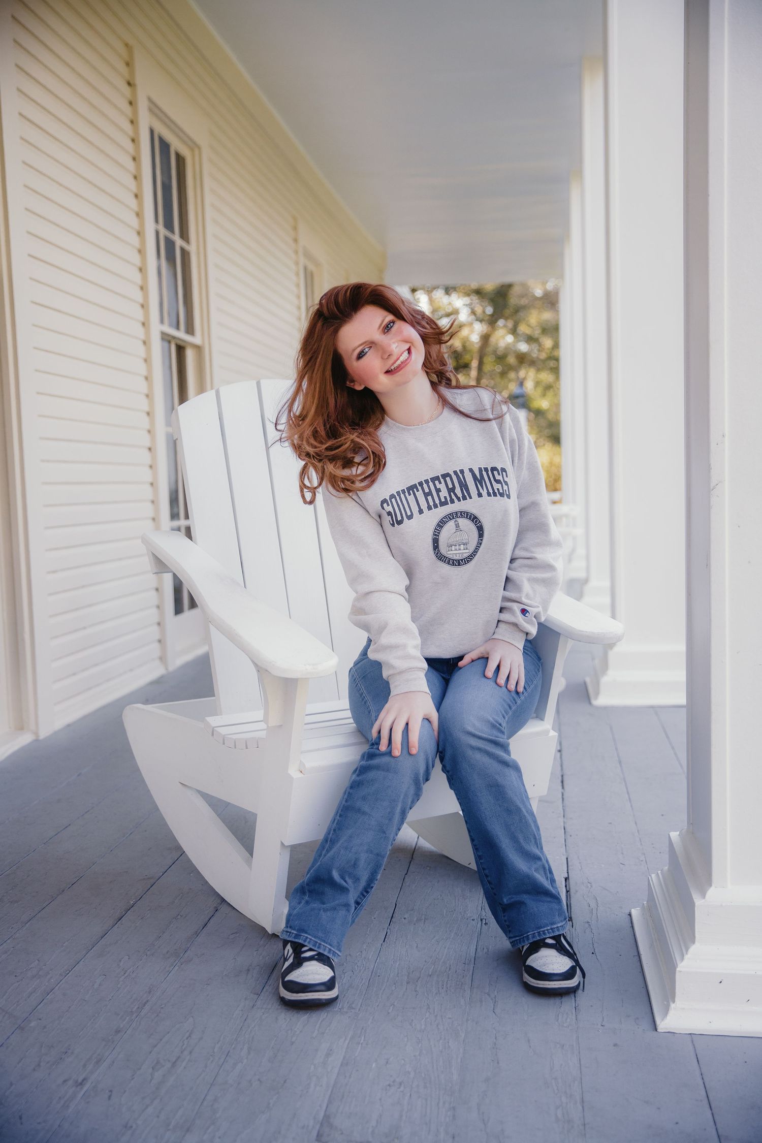 Someone lounging in a white Adirondack chair wearing a collegiate sweatshirt and jeans.