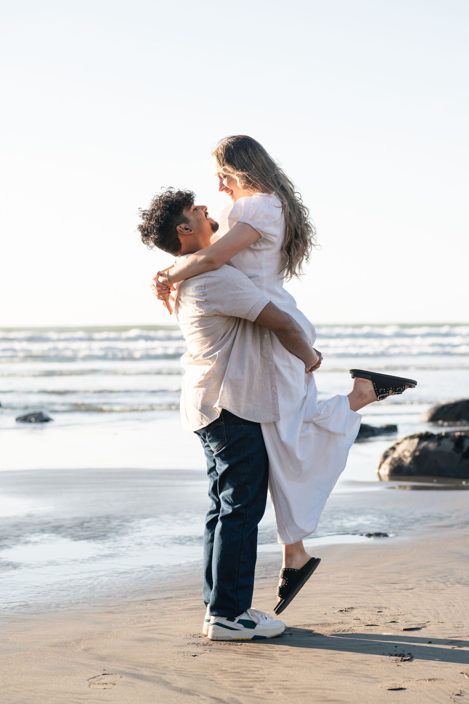 Happy couple in white clothes sharing a joyful moment on a sunny beach Raglan New Zealand