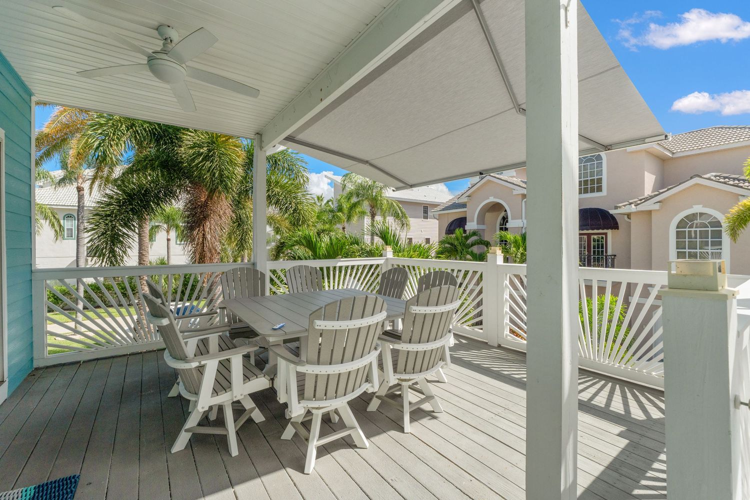White deck with comfortable seating overlooking palm trees and luxury homes in a residential community.
